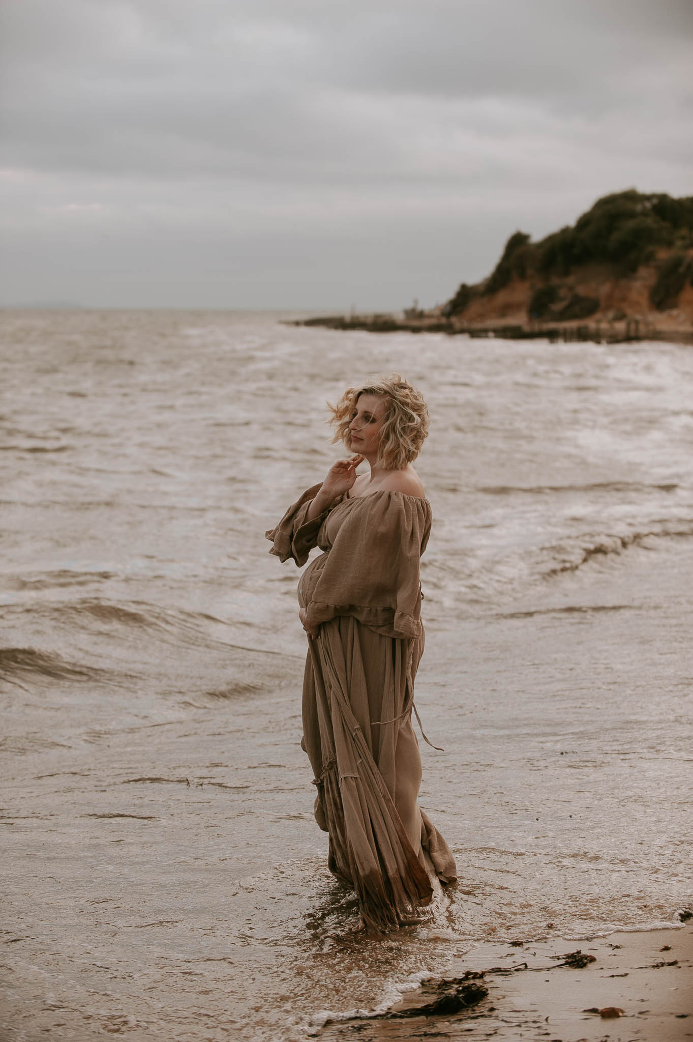 A pregnant woman in a long dress standing in the water at Lepe Beach in the New Forest.